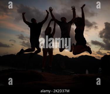 Springen vor Freude. Aufnahme einer Gruppe von springenden Freunden, die gegen einen Sonnenuntergang gedreht wurden. Stockfoto