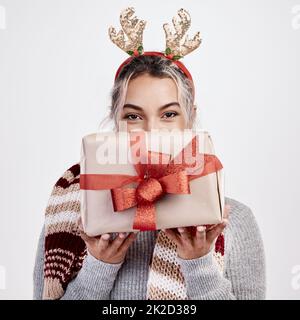 Für mich. Studioporträt einer attraktiven jungen Frau, die ein Geschenk vor ihrem Gesicht hält, während sie in weihnachtlicher Kleidung gekleidet ist. Stockfoto