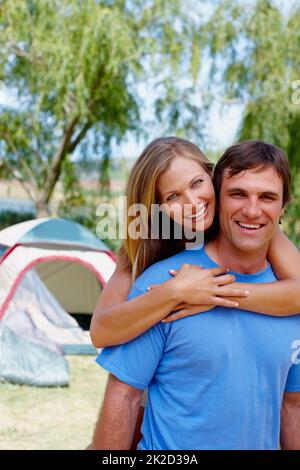 Liebevolles Paar. Porträt eines Paares, das mit einer Frau zeltet, die den Mann von hinten umarmt. Stockfoto