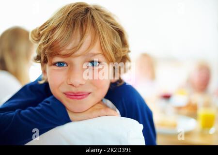 Glücklicher kleiner Junge und seine Familie beim Frühstück im Hintergrund. Nahaufnahme eines glücklichen Jungen und seiner Familie beim Frühstück im Hintergrund. Stockfoto