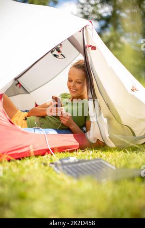 Handy wird während einer Fahrt im Freien mit einem Solarladegerät in einem Zelt aufgeladen Stockfoto