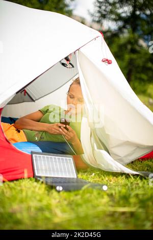 Handy wird während einer Fahrt im Freien mit einem Solarladegerät in einem Zelt aufgeladen Stockfoto