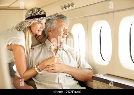 Eine Luxusreise machen. Lächelndes Seniorenpaar in einem Flugzeug, das aus dem Fenster schaute. Stockfoto