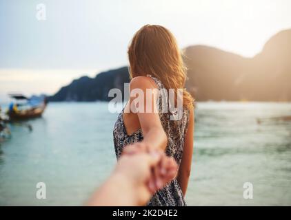 Folge mir ins Paradies. Aufnahme einer jungen Frau, die jemanden an der Hand am Strand führt. Stockfoto