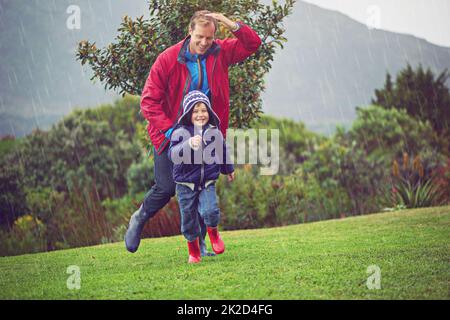 Schnell, kommen wir hier raus. Ganzkörperaufnahme eines Vaters und seines Sohnes, die im Regen draußen laufen. Stockfoto