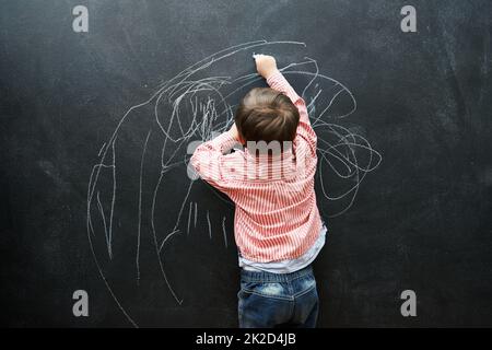 Eines Tages wird sich diese Ziehung für Millionen verkaufen. Ein kleiner Junge, der auf einer Tafel zeichnet. Stockfoto