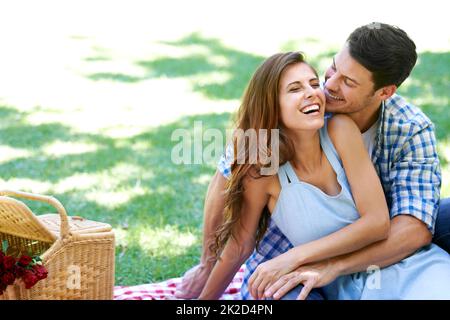 Lachend und liebevoll im Park. Ein glückliches junges Paar genießt ein Picknick in der Sommersonne. Stockfoto