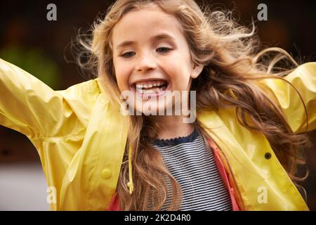 Quietscht vor Freude. Aufnahme eines niedlichen kleinen Mädchens, das einen Regenmantel trägt und draußen spielt. Stockfoto