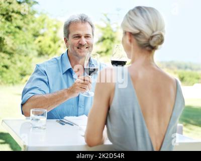 Genießen Sie ein Mittagessen Datum. Glückliches reifes Paar, das seine Liebe mit zwei Gläsern Wein im Freien toaste. Stockfoto