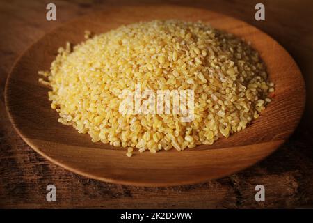 Trockener Bulgurweizen in Holzschüssel isoliert verschüttete Bulgur Stockfoto