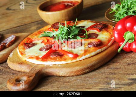 Hot hausgemachte Pizza mit Salami, paprica, Rucola auf hölzernen Tisch Stockfoto