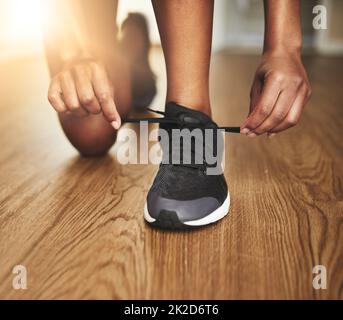 Mach dich bereit, so zu laufen, wie dein Leben davon abhängt. Kurzer Schuss einer jungen Frau, die ihre Schnürsenkel bindet. Stockfoto