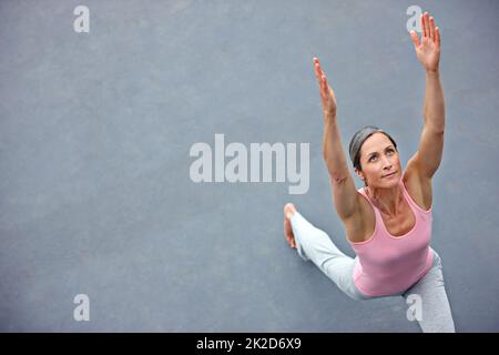 Sich frei und flexibel fühlen. High-Angle-Aufnahme einer attraktiven reifen Frau, die im Freien Yoga macht. Stockfoto