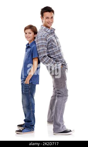 Sie sind zwei coole Jungs. Ein Vater und ein Sohn stehen vor einem weißen Hintergrund Rücken an Rücken. Stockfoto