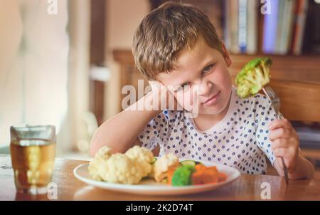 Es gibt keine Möglichkeit, diese Sachen zu essen. Porträt eines angewiderten kleinen Jungen, der sich weigert, sein Gemüse am Esstisch zu essen. Stockfoto