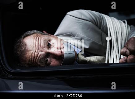 Helft mir... Porträt eines verängstigten Geschäftsmannes, der gebunden und geknebelt im Kofferraum eines Autos liegt. Stockfoto