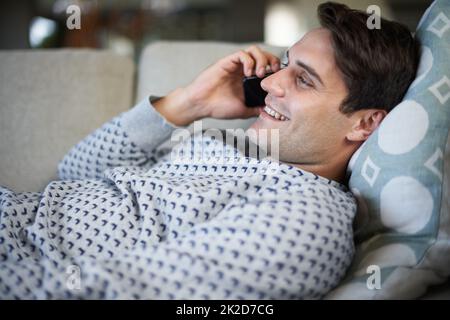 Nein zu den Jungs sagen und sich entscheiden, auf der Couch zu bleiben. Aufnahme eines jungen Mannes, der auf seinem Sofa lag, während er am Telefon sprach. Stockfoto