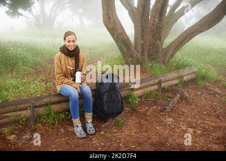 Sich in der wunderschönen Umgebung ausruhen. Porträt einer jungen Wanderin, die an einem Baum auf einem Wanderweg sitzt. Stockfoto