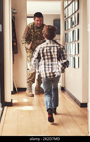 Raten Sie mal, wer nach Hause kommt. Rückansicht eines kleinen Jungen, der seinen Vater begrüßt, als er aus der Armee zurückkehrt. Stockfoto