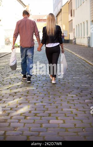 Hand in Hand. Ein glückliches junges Paar, das Hand in Hand durch die Straßen geht. Stockfoto