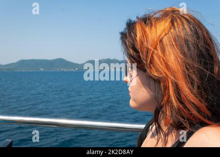 Eine Frau mit orangefarbenem Schwarz, die auf einem Kreuzfahrtschiff sitzt und auf das Meer schaut Stockfoto