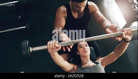 Shes verpflichtet sich, ihre Fitnessziele zu erreichen. Aufnahme einer fokussierten jungen Frau, die Gewichte hebt und ihr persönlicher Trainer dabei hilft. Stockfoto