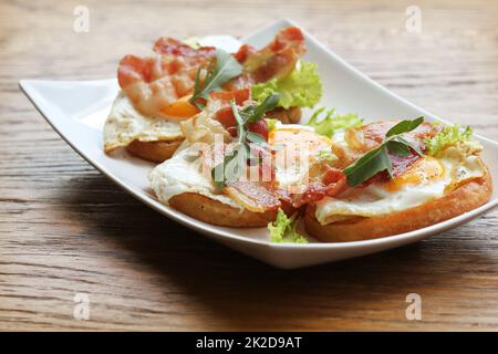 Bruschetta mit Rucola, chrispy Speck und pochiertem Ei auf einem weißen Teller serviert Stockfoto