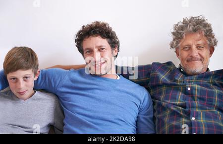 Jahrzehntelanger Unterschied. Porträt von drei Generationen von Männern, die zu Hause auf einem Sofa sitzen. Stockfoto