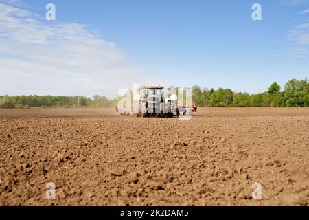 Das Land säen. Aufnahme eines Traktors, der ein großes gepflügeltes Feld auf einem Bauernhof sät. Stockfoto