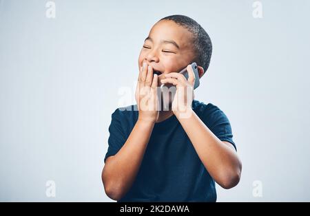 Ein Anruf von Oma gibt ihm immer das Kichern. Studio-Aufnahme eines niedlichen kleinen Jungen, der erstaunt mit einem Smartphone vor einem grauen Hintergrund aussieht. Stockfoto