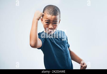 Diese Waffen wachsen von Tag zu Tag. Studioaufnahme eines niedlichen kleinen Jungen, der seine Muskeln vor einem grauen Hintergrund beugend. Stockfoto