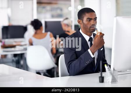 Sein Problem zu beheben, ohne seinen Schreibtisch zu verlassen. Ein junger Geschäftsmann, der drinnen eine elektronische Pfeife raucht. Stockfoto