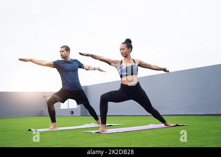 Die Wahrung von Gleichgewicht und Form ist der Schlüssel. Aufnahme eines jungen Mannes und einer jungen Frau, die gemeinsam im Freien Yoga praktizieren. Stockfoto