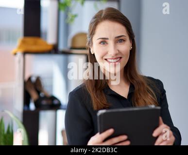 Mein Geschäft boomt auch online. Porträt einer jungen Geschäftsbesitzerin, die in ihrem Bekleidungsgeschäft ein digitales Tablet benutzt. Stockfoto