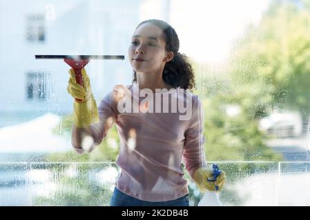 Man kann sich keinen einzigen Ort entgehen lassen. Aufnahme einer jungen Frau, die zu Hause ihr Fenster putzt. Stockfoto