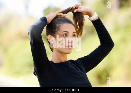 Stellen Sie sicher, dass ihr Haar nicht im Weg steht. Eine kurze Aufnahme einer attraktiven und athletischen jungen Frau, die ihre Haare im Freien bindet. Stockfoto