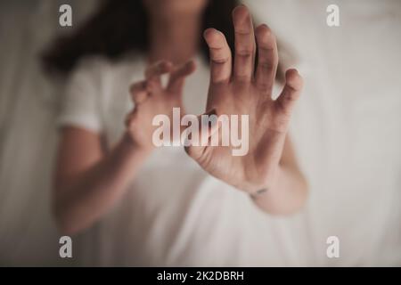 Schadet nicht zuerst. In einem hohen Winkel eine unidentifizierbare junge Frau, die ihre Hände in einer defensiven Geste hochhält, während sie im Bett liegt. Stockfoto