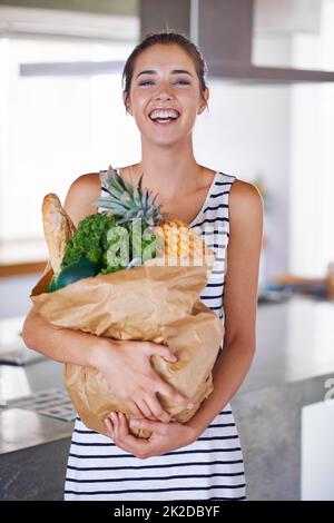 Ein gesundes Leben ist ein glückliches Leben. Eine attraktive Frau, die eine Tüte Lebensmittel in der Küche hält. Stockfoto