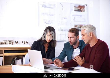 Verwendung der neuesten Computersoftware für ihre Designs. Eine kurze Aufnahme von drei Architekten, die an einem neuen Gebäudedesign arbeiten. Stockfoto