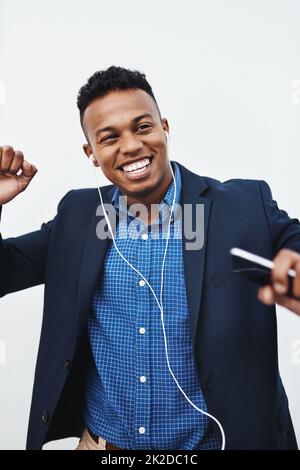 Beenden Sie Ihren Tag immer mit einem hohen Ton. Studioaufnahme eines jungen kreativen Geschäftsmannes, der Musik auf seinem Handy vor grauem Hintergrund hört. Stockfoto