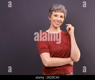 Lächeln Sie, es lohnt sich. Studioporträt einer selbstbewussten älteren Frau vor grauem Hintergrund. Stockfoto