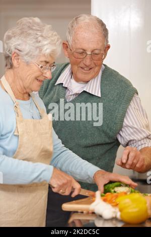 Hes immer an meiner Seite... sogar in der Küche. Eine Aufnahme eines älteren Paares, das zusammen eine Mahlzeit zubereitet. Stockfoto