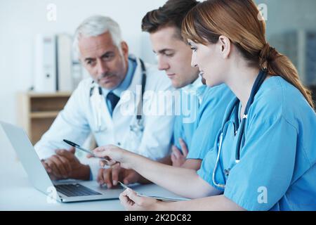 Wichtiges medizinisches Treffen wird durchgeführt. Aufnahme von drei medizinischen Fachkräften, die über einen Laptop diskutieren. Stockfoto