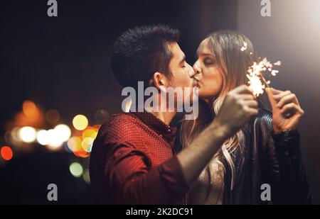 Die Funken fliegen, wenn wir uns küssen. Aufnahme eines glücklichen jungen Paares, das nachts mit Wunderkerzen gefeiert hat. Stockfoto