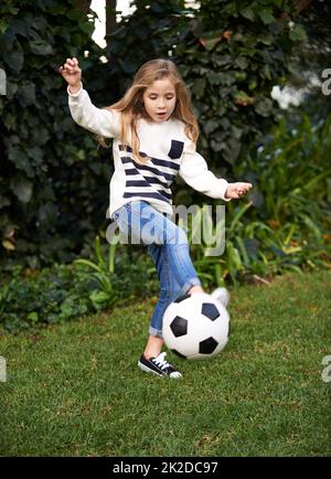 Shes hat etwas Geschick. Aufnahme eines kleinen Mädchens, das mit einem Fußball in einem Garten spielt. Stockfoto