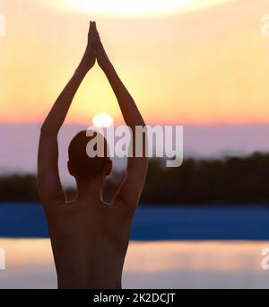 Ruhe in der Natur finden. Eine schöne junge Frau in einer Yoga-Pose bei Sonnenuntergang. Stockfoto