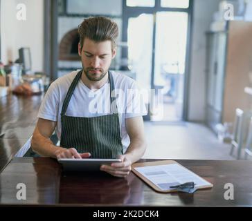 Alles auf Knopfdruck. Ein kurzer Screenshot eines jungen Barista, der ein Tablet in seinem Coffee Shop verwendete. Stockfoto