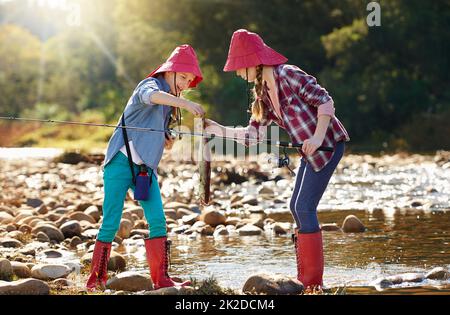 Angelfreunde, die Spaß haben. Aufnahme von zwei jungen Mädchen, die an einem Fluss fischen. Stockfoto