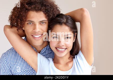 Glück und Liebe. Studioporträt eines fröhlichen jungen ethnischen Paares, das die Kamera umarmt und lächelt. Stockfoto