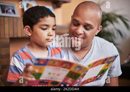 Jetzt sind Sie an der Reihe zu lesen. Eine kurze Aufnahme eines fröhlichen kleinen Jungen und seines Vaters, der tagsüber zu Hause ein Geschichtenbuch liest. Stockfoto